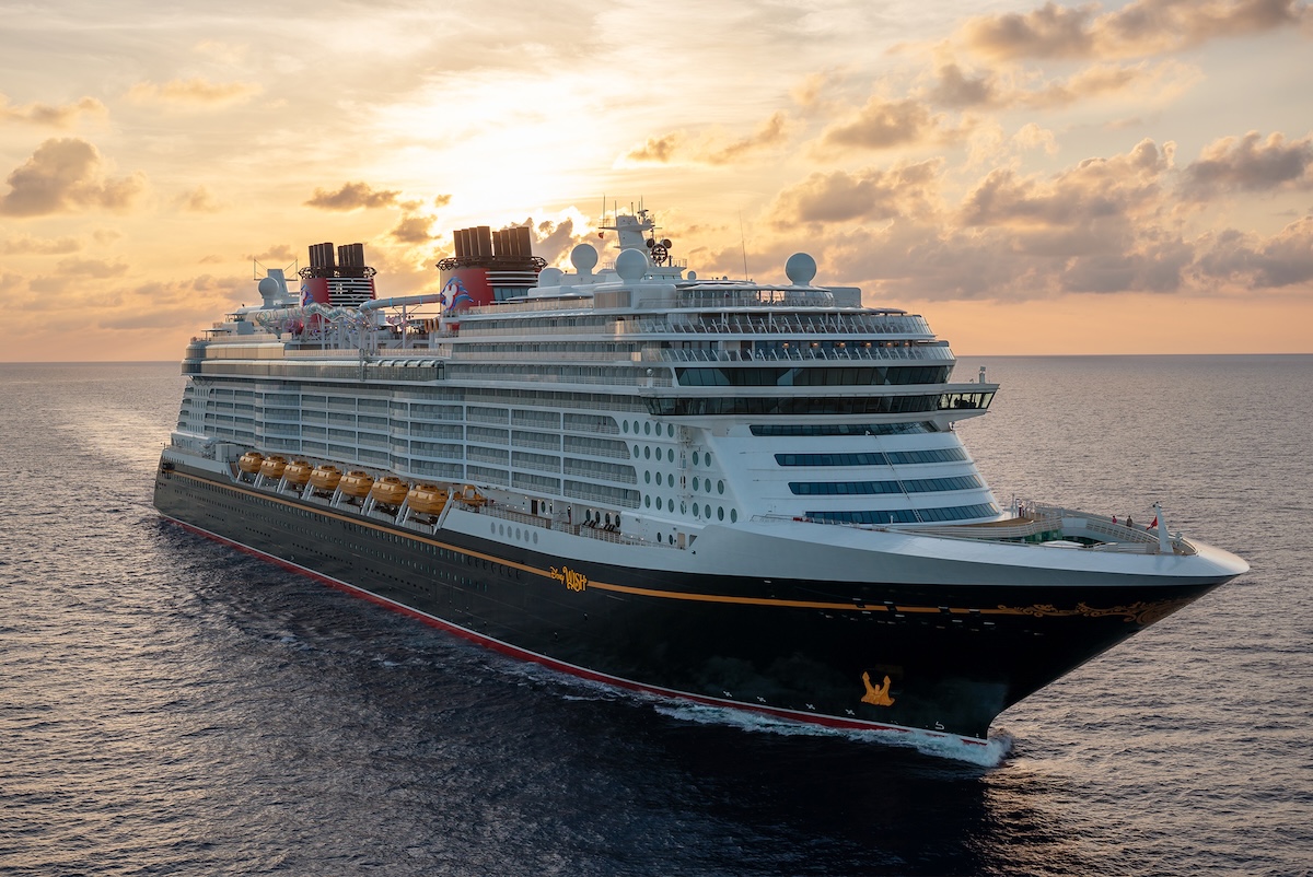 A cruise ship, in the style of a classic ocean liner, moves across the ocean, with a bright sunset just behind the ship.